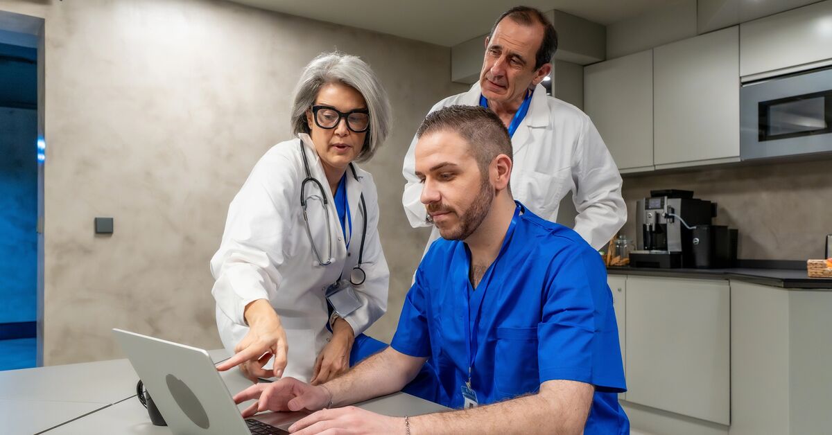 Medical professionals in scrubs and lab coats collaborating on a laptop, sharing information, and discussing healthcare data