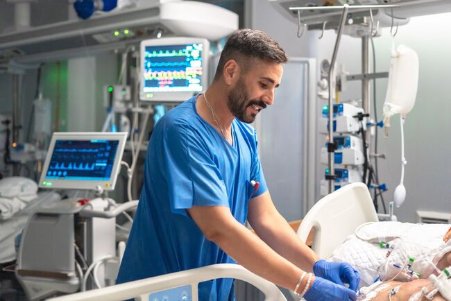 Male healthcare professional in blue scrubs providing care to a patient in the icu